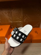Hermes slide sandals held up; white sole with black strap featuring repeating H icons