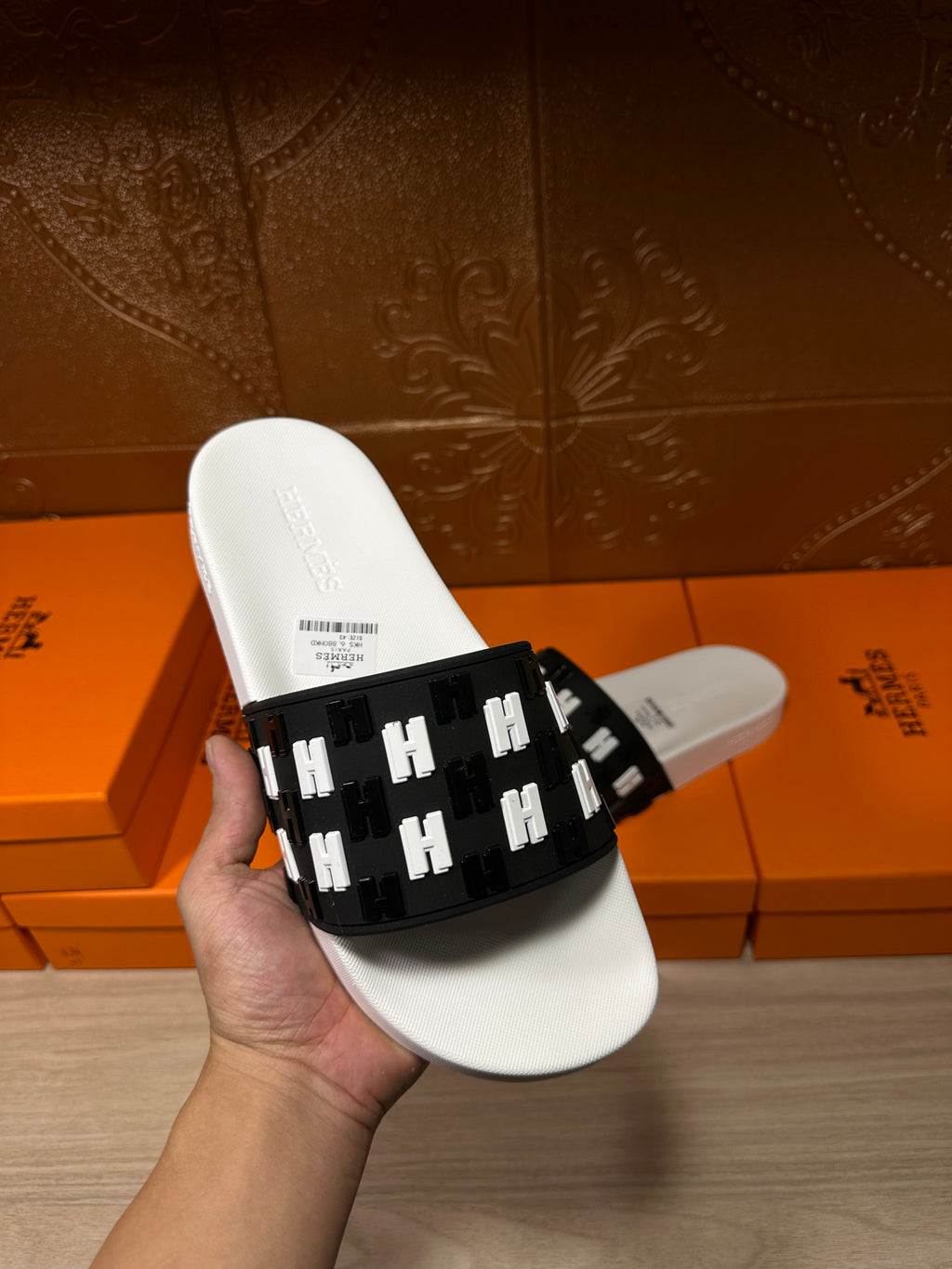 Hermes slide sandals held in hand; white footbed with black H-logo strap