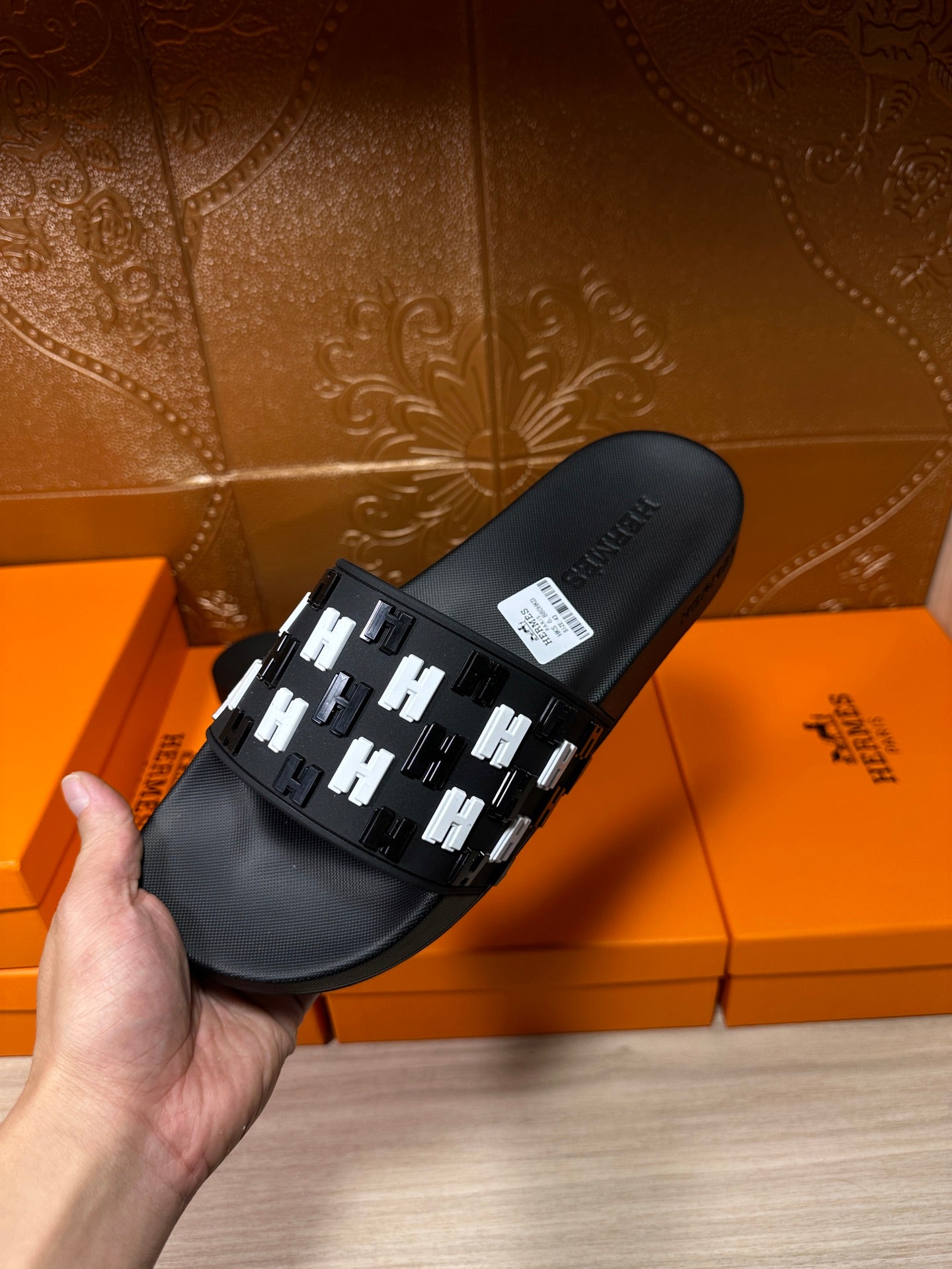 Black slide sandal held in hand, showing white patterned strap over footbed
