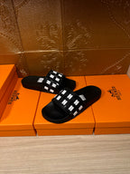 Black slide sandals resting on orange boxes, featuring a white patterned strap
