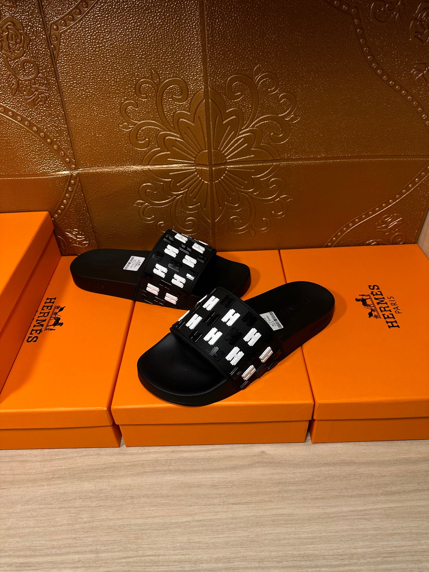 Black slide sandals resting on orange boxes, featuring a white patterned strap