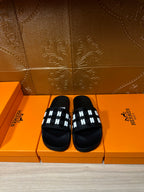 Black slide sandals with white patterned strap across the toe