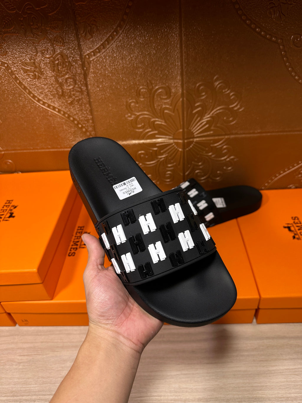 Black slide sandal held by a hand, featuring a white patterned strap