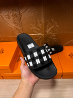 Black slide sandal held by a hand, featuring a white patterned strap