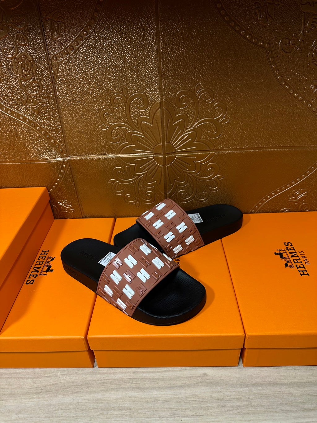 Hermes slide sandals with tan strap and white repeating H pattern, black slide soles