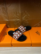 Hermes slide sandals with tan strap and white repeating H pattern, black slide soles