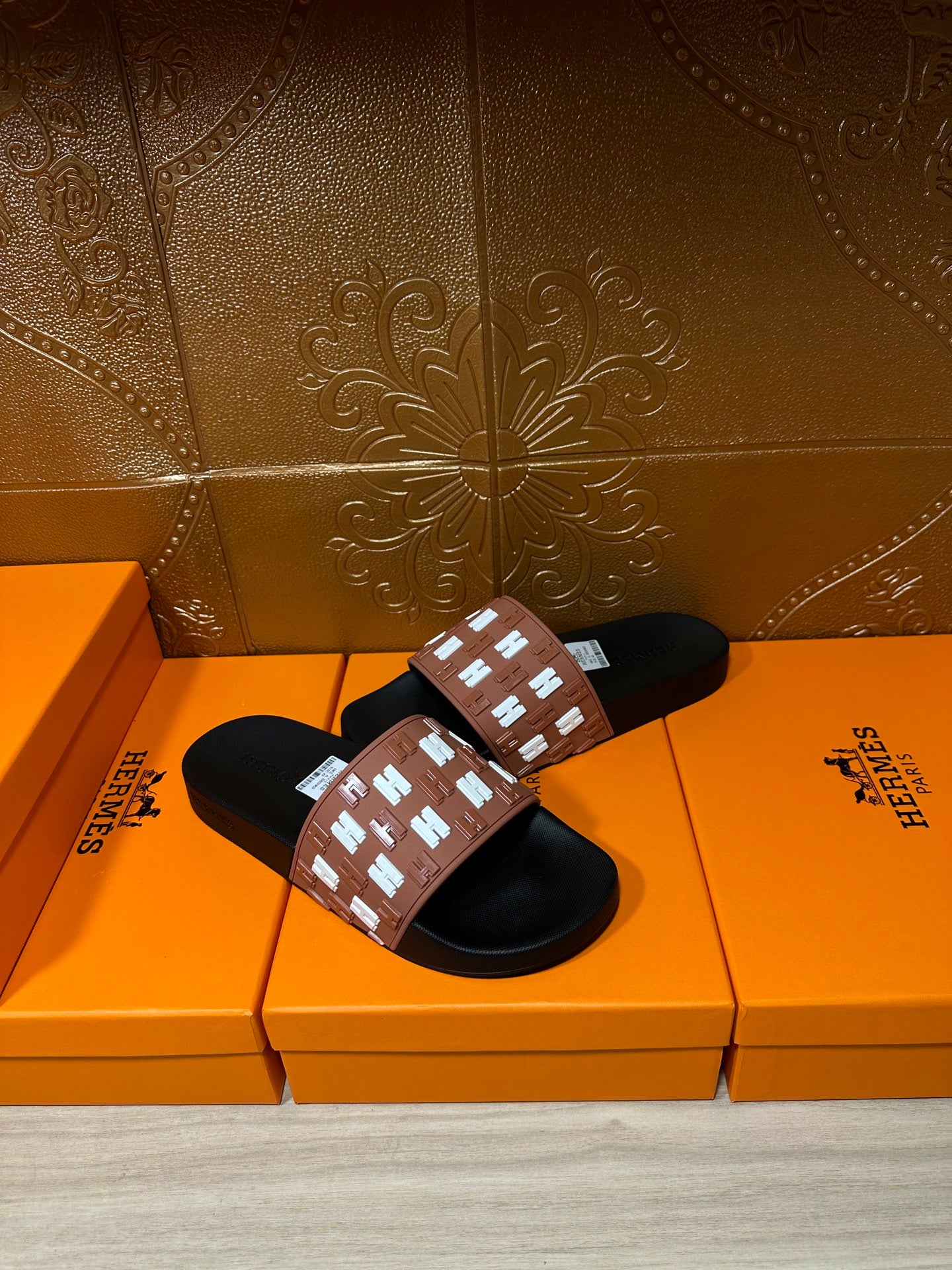 Hermes slide sandals with tan strap and white repeating H pattern, black slide soles