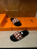 Hermes slide sandal held in hand, black sole and tan strap with white H pattern