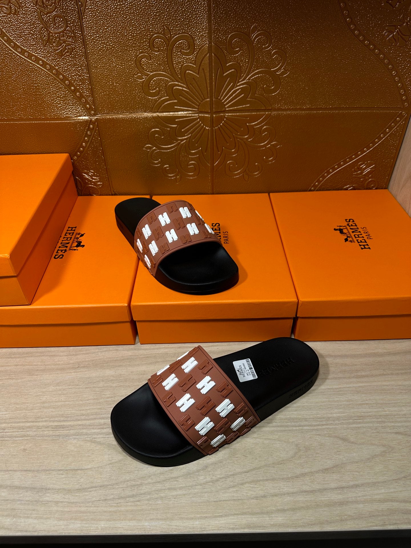 Hermes slide sandal held in hand, black sole and tan strap with white H pattern