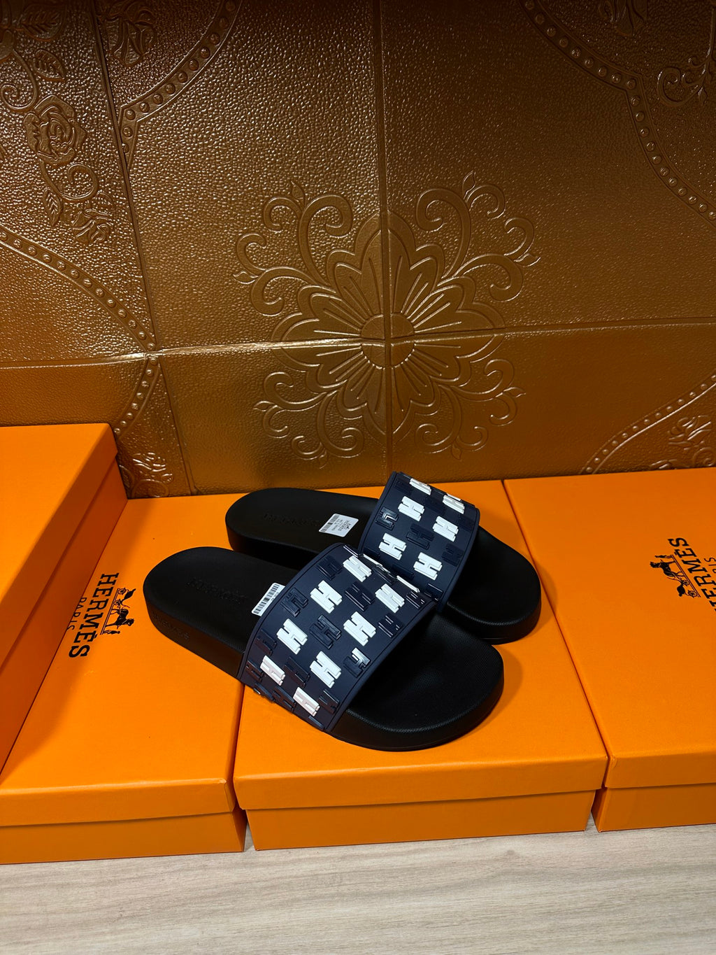 Black and navy slide sandals with repeating white H trim on strap