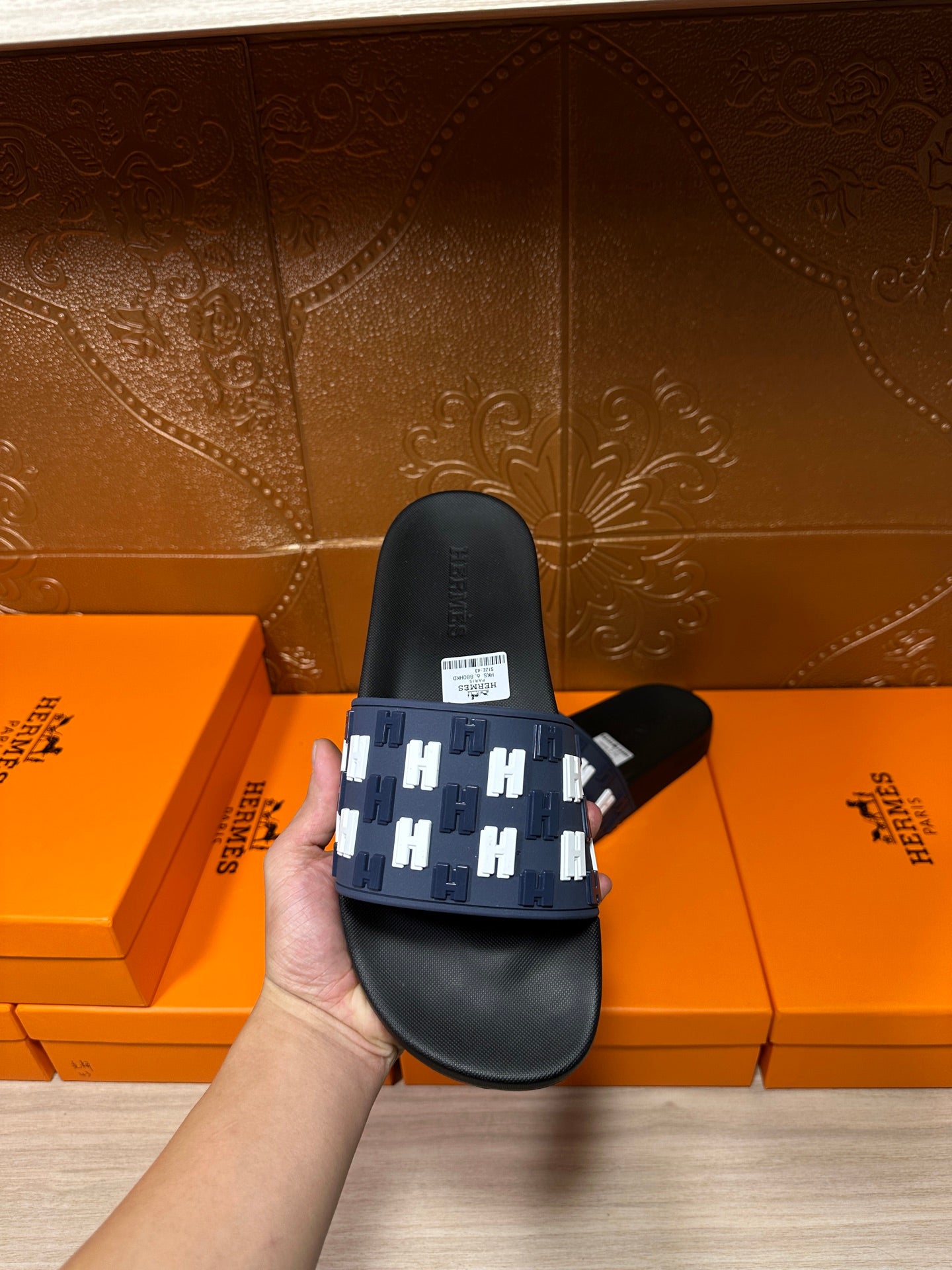 Black slide sandal with navy strap and white H pattern, heel view