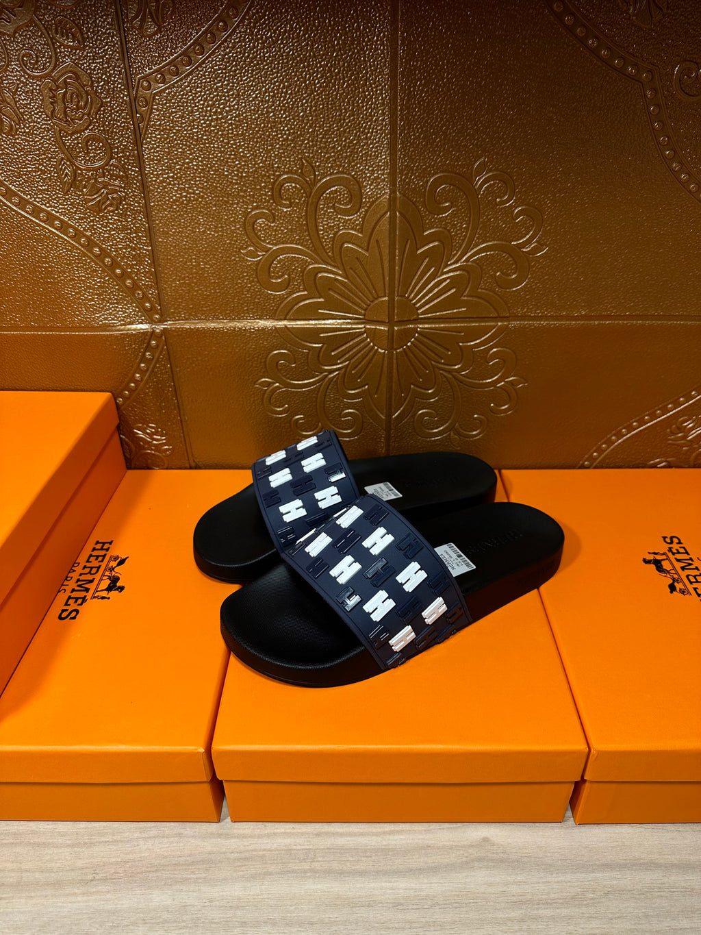 Black slide sandals with navy strap featuring repeating white H logo