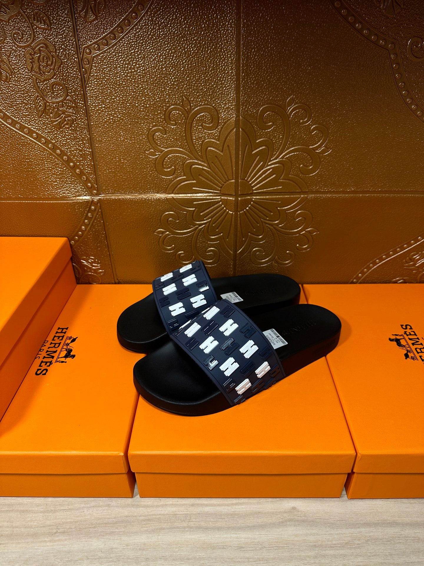 Black slide sandals with navy strap featuring repeating white H logo