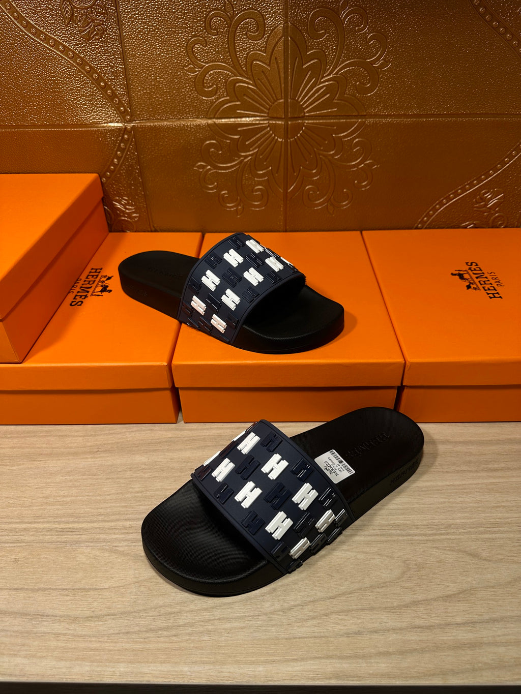 Black slide sandals with navy patterned strap and white H detail