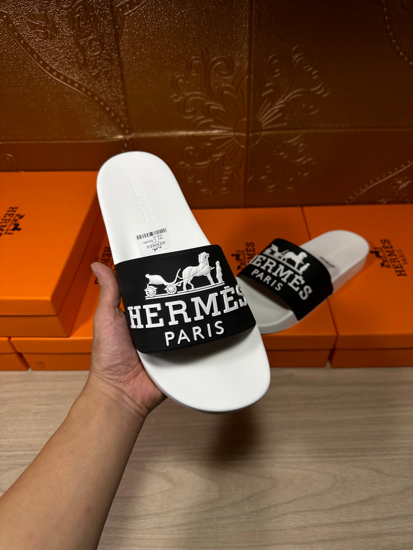 Hand holding Hermes slide sandal with white footbed and black Hermes Paris strap