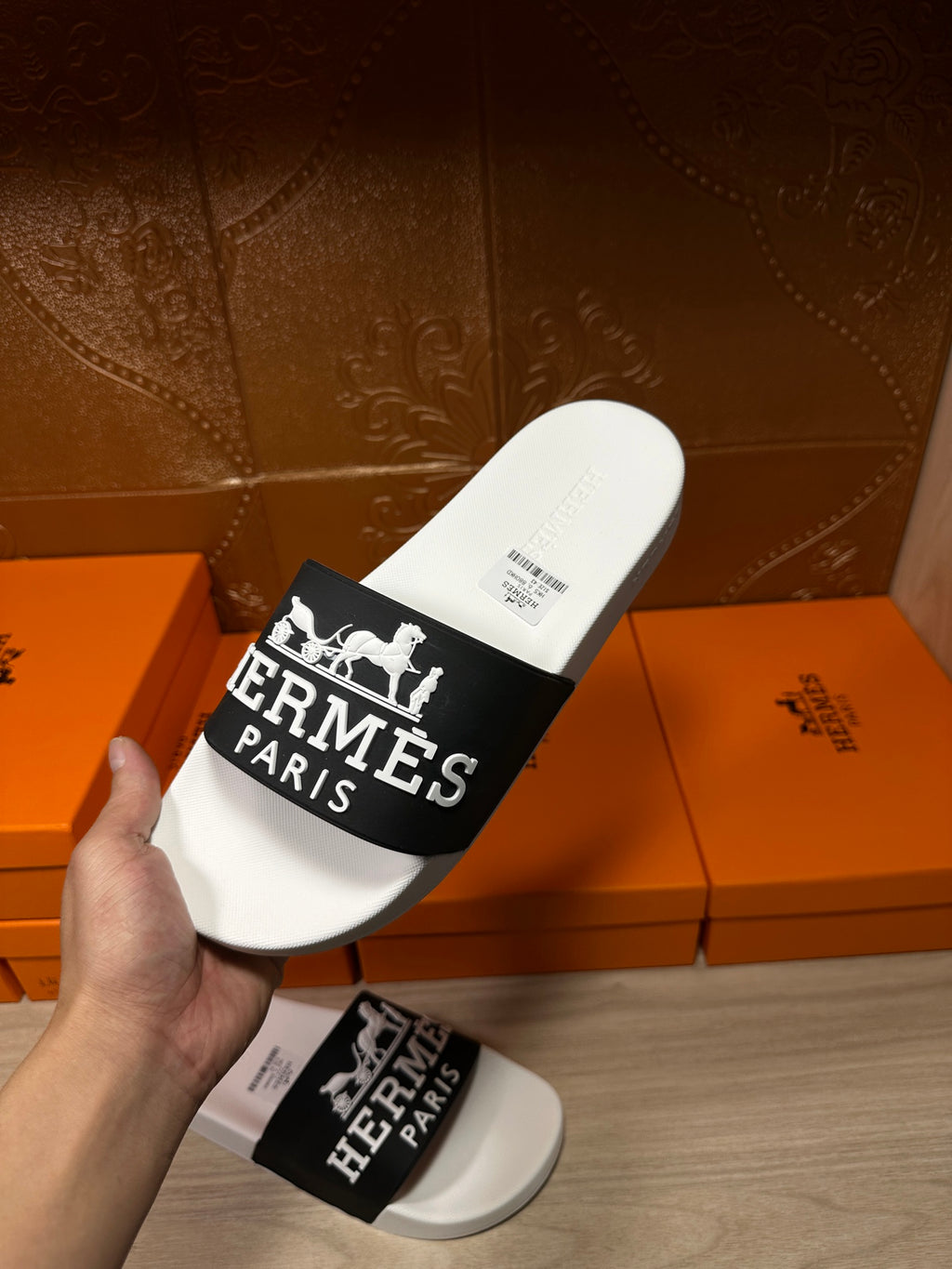Hand holding Hermes slide sandal with white footbed and black Hermes Paris logo