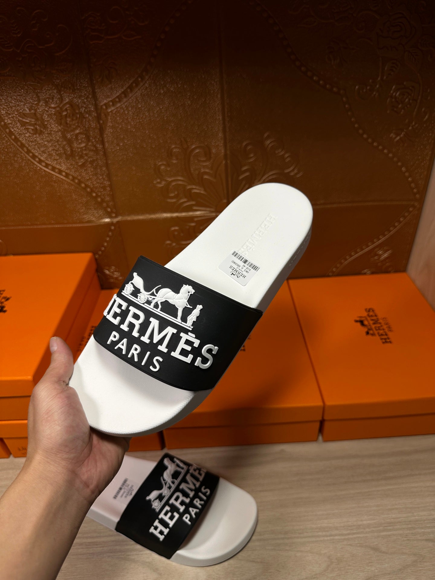 Hand holding Hermes slide sandal with white footbed and black Hermes Paris logo