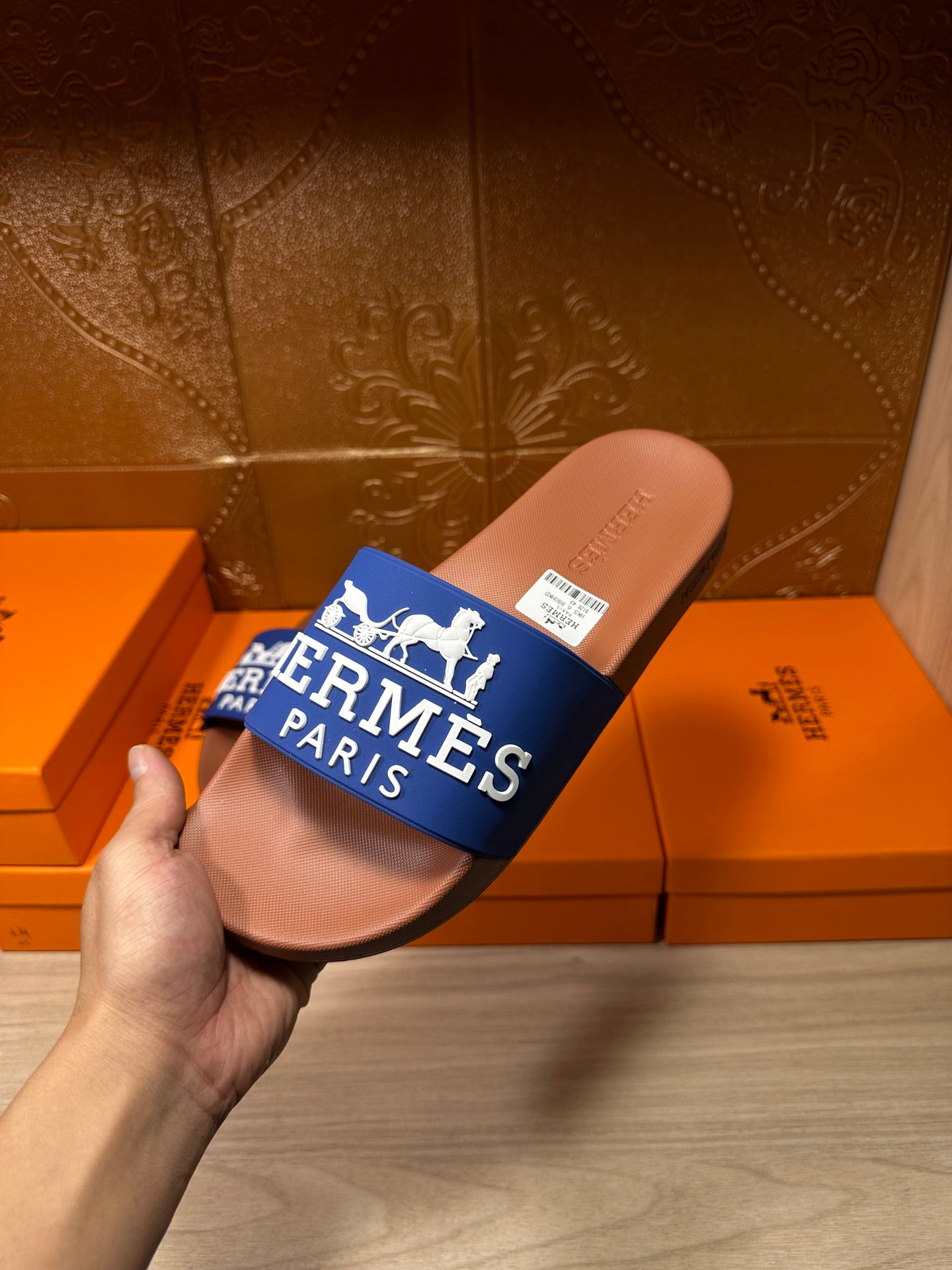 Hand holding brown slide sandal with blue Hermes Paris strap, close-up