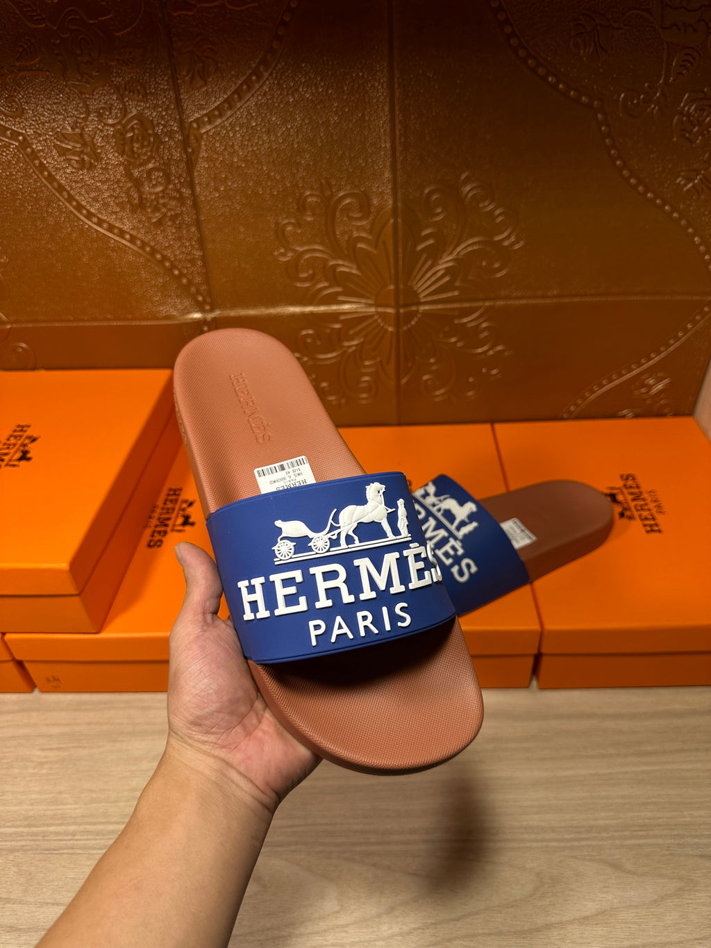 Hand holding brown slide sandal with blue Hermes Paris strap