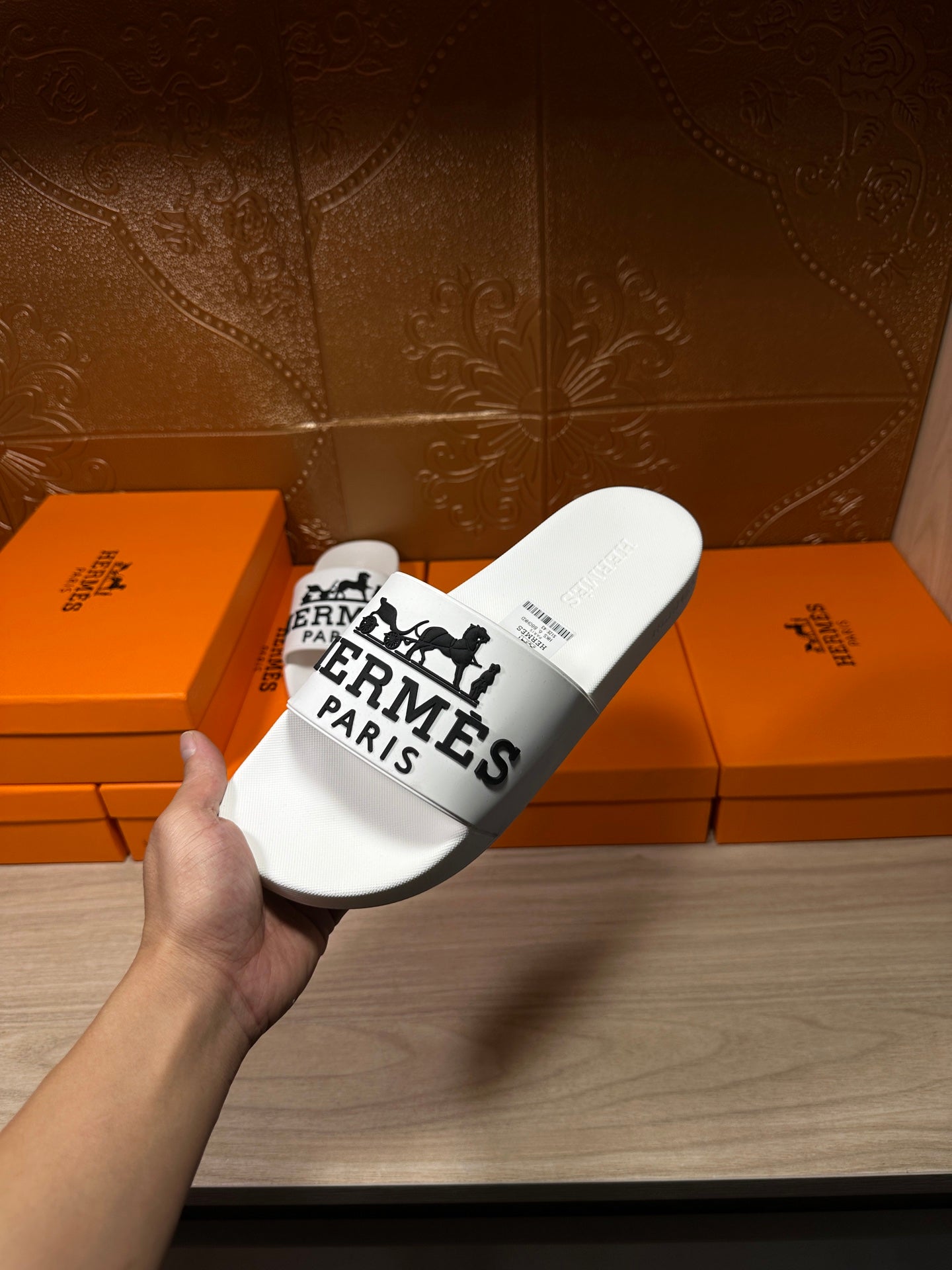 White slide sandal held in hand with black Hermes Paris logo strap