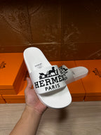 White slide sandal held in hand with Hermes Paris logo strap