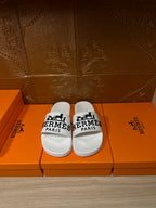 White slide sandals with black Hermes Paris logo straps