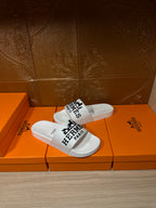 White slide sandals showing Hermes Paris printed strap