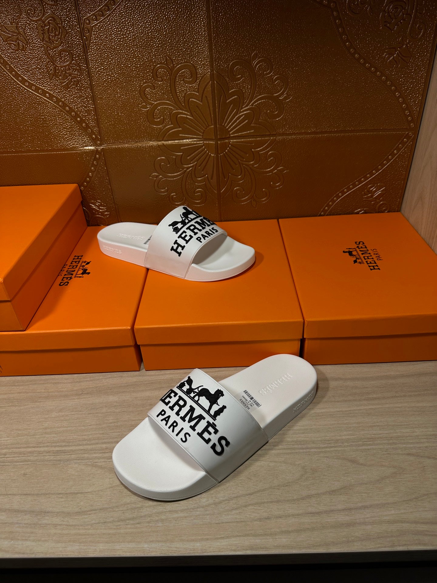 White slide sandals with black Hermes Paris logo on orange box display