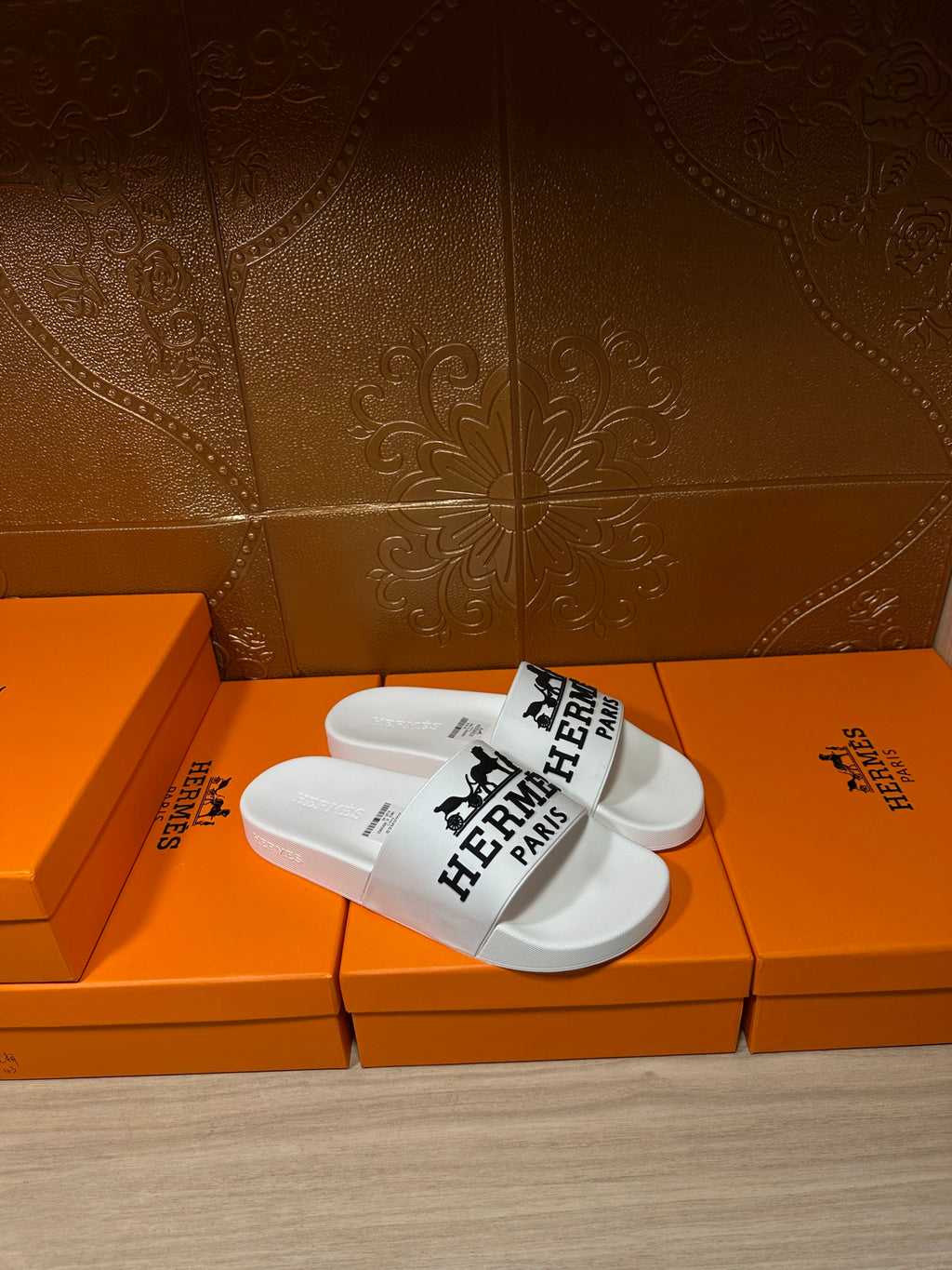White slide sandals with black Hermes Paris logo across the strap