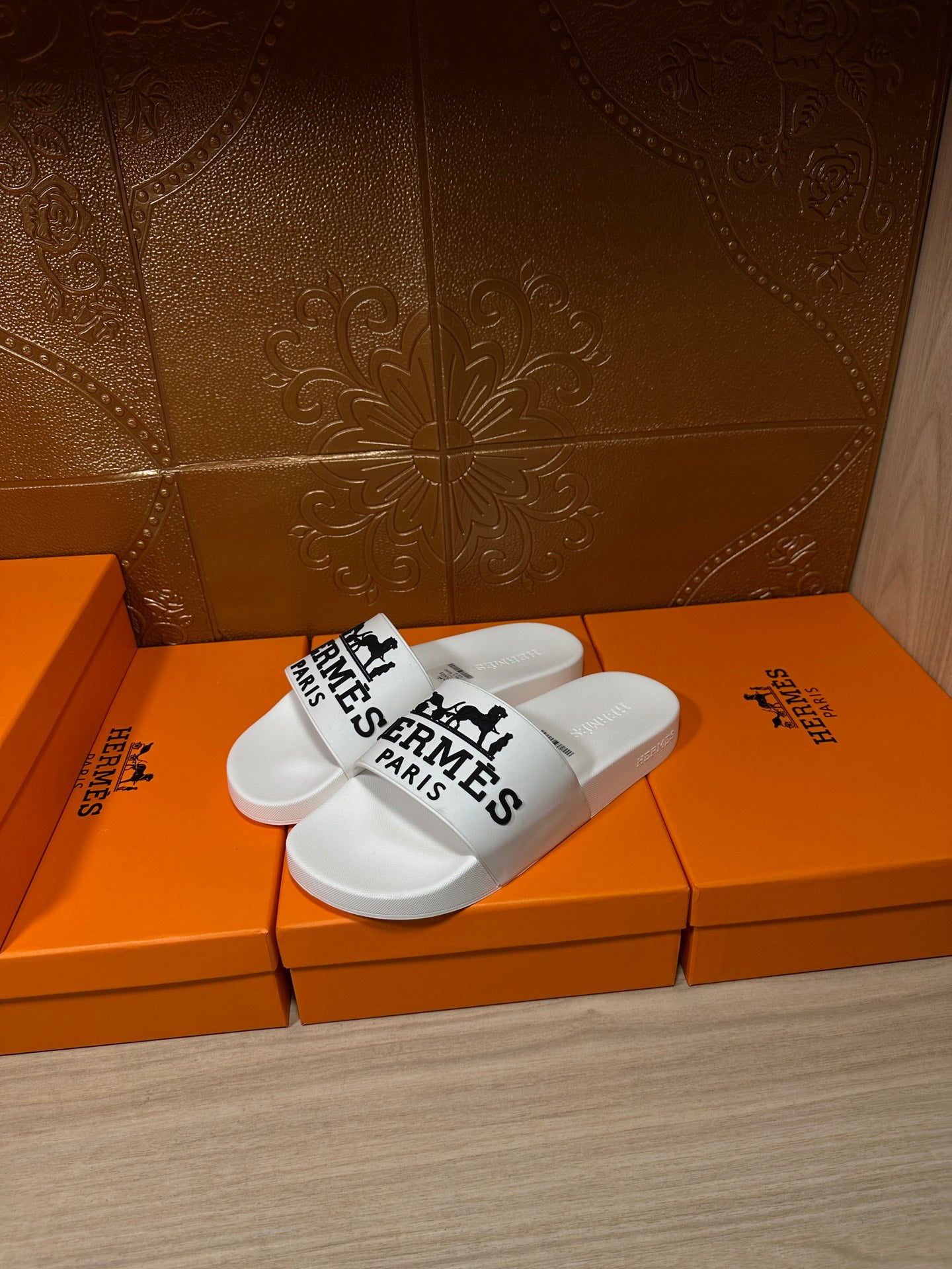 White slide sandals with black Hermes Paris logo straps on orange boxes