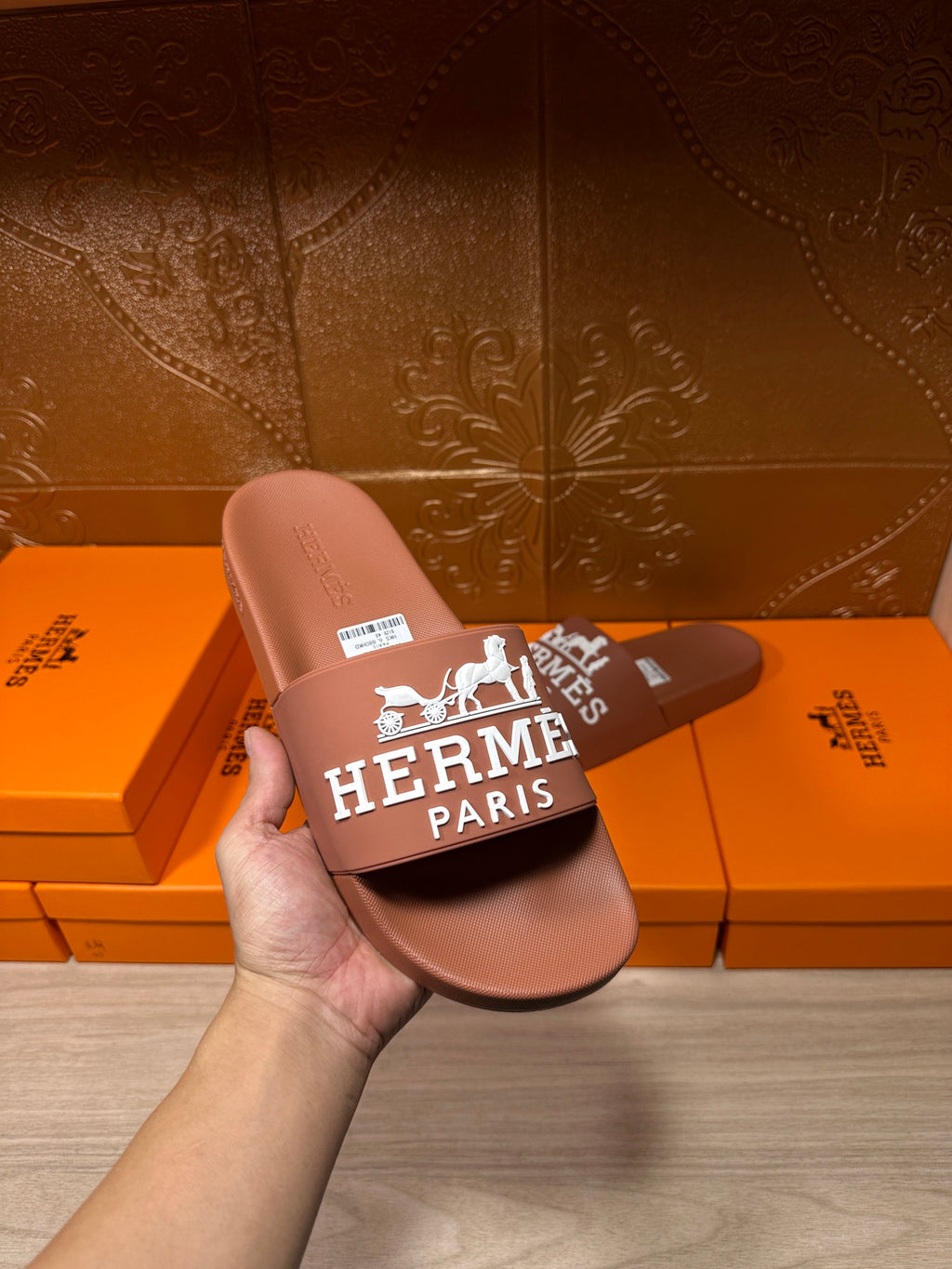 Brown slide sandal held in hand, white HERMES PARIS logo strap