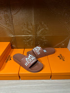 Brown slide sandals with white HERMES PARIS logo strap, front view