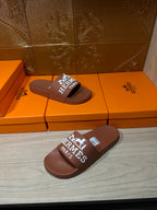 Brown slide sandals on floor, white HERMES PARIS logo strap