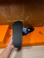 Black slide sandal outsole with textured tread, showing blue Hermes Paris strap.