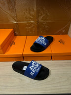 Black slide sandals with blue Hermes Paris strap, set on orange retail boxes.