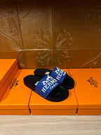 Black slide sandals with blue Hermes Paris strap, sandals resting on orange boxes.