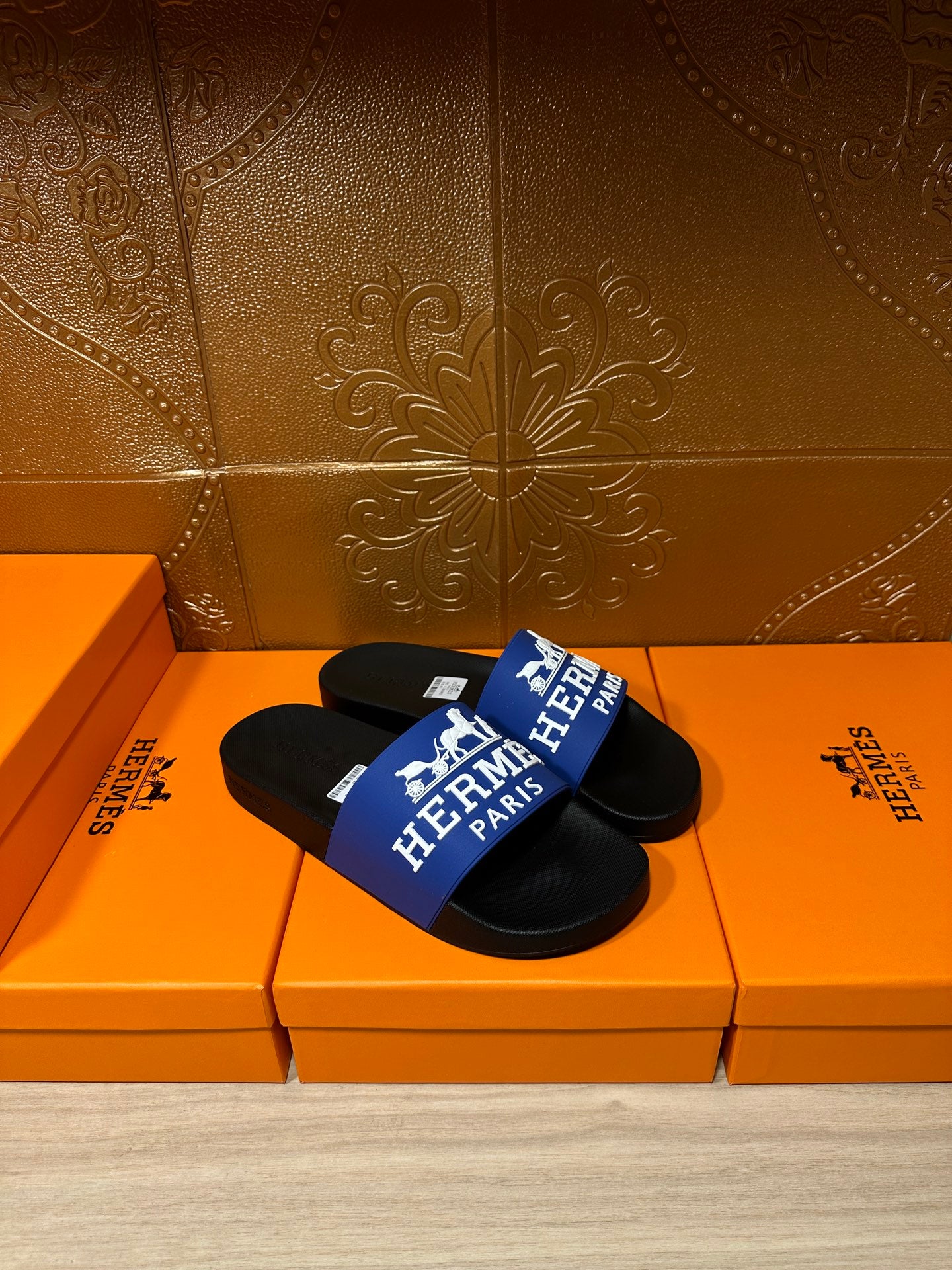 Black slide sandals with blue Hermes Paris strap, sandals resting on orange boxes.