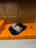 Black Hermes slide sandals with tan logo strap, single sandal resting on box