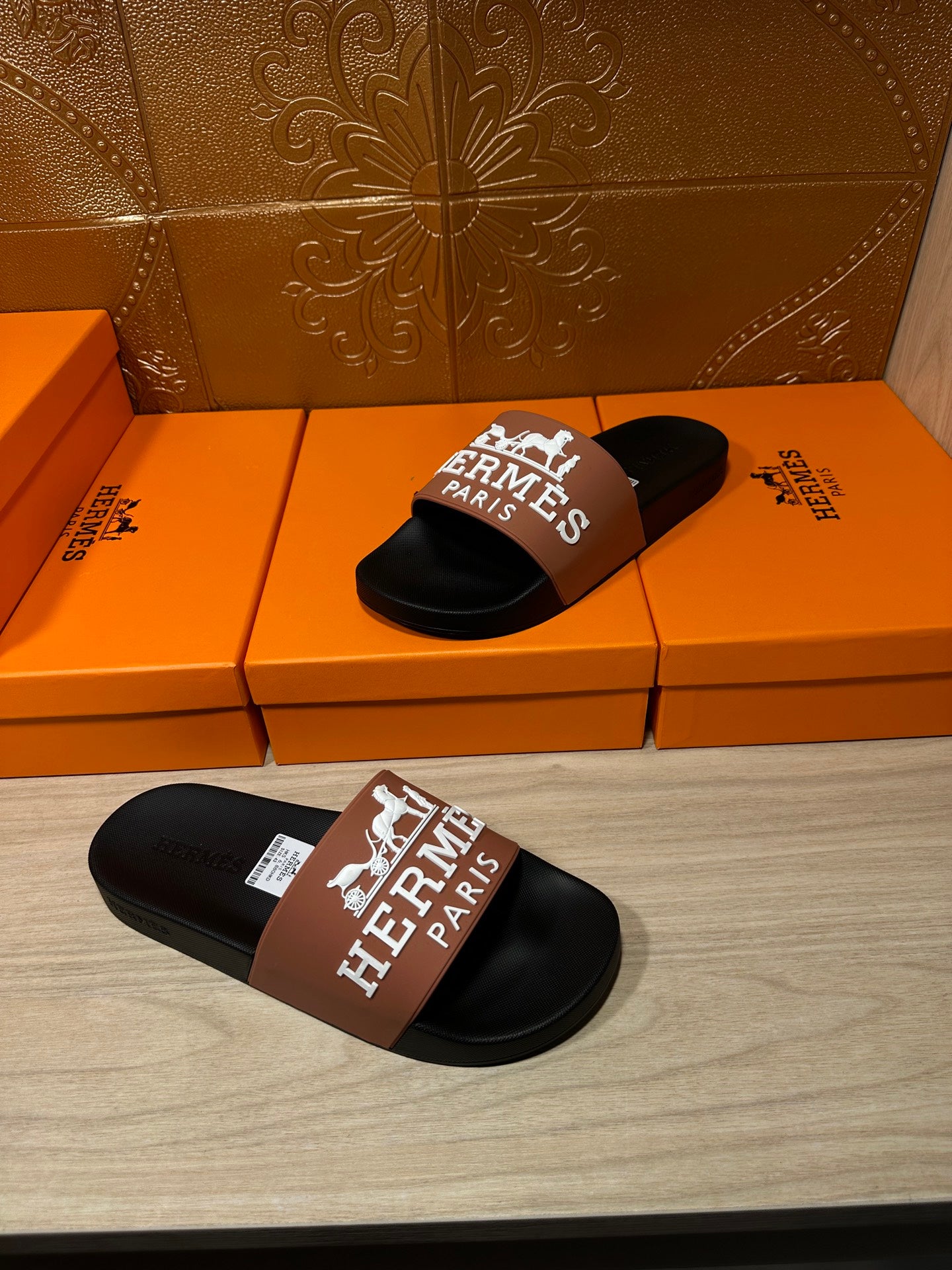 Black slide sandals with tan Hermes Paris logo strap, one sandal on foreground