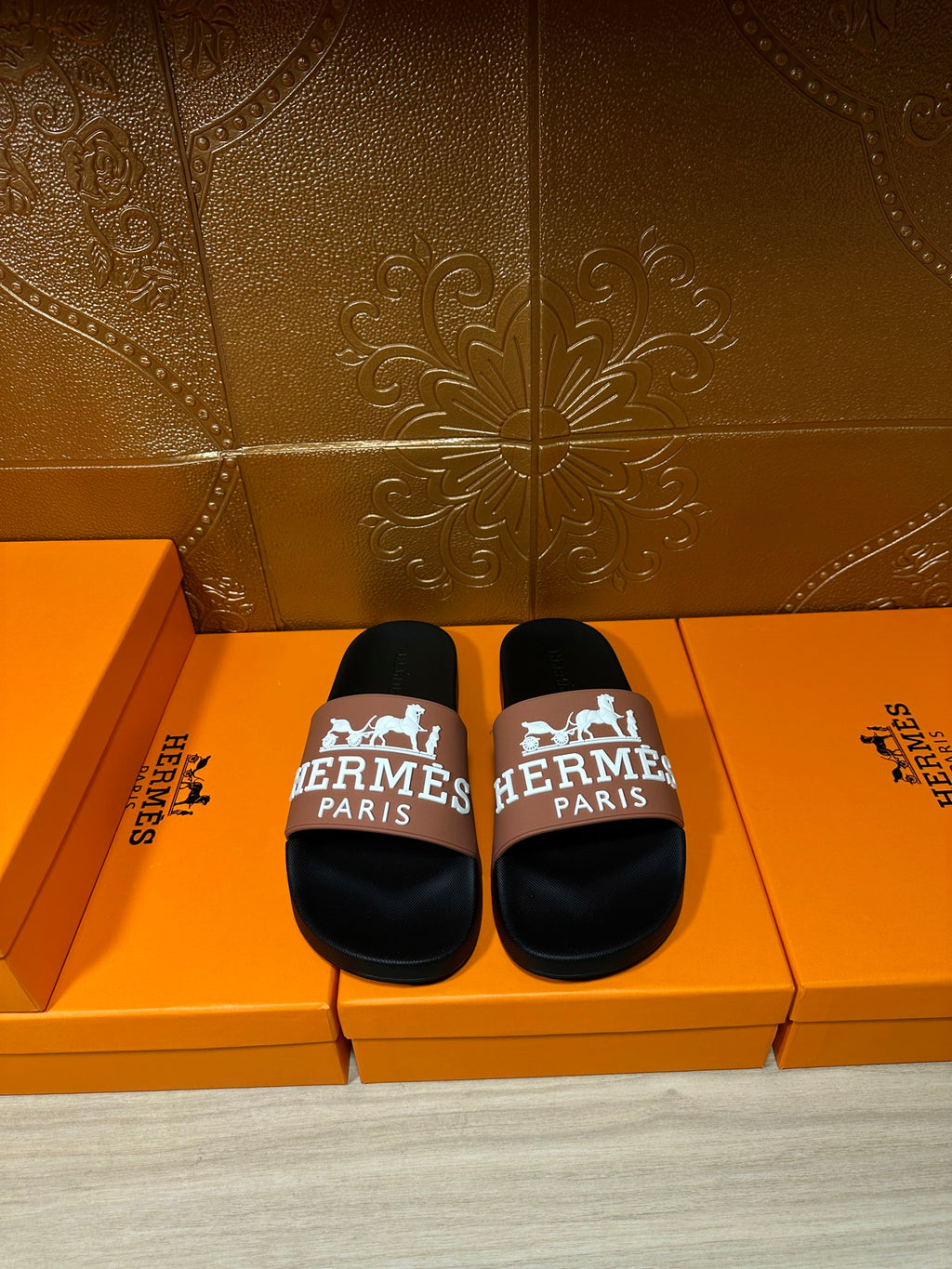 Black slide sandals with tan strap featuring Hermes Paris logo, shown as a pair
