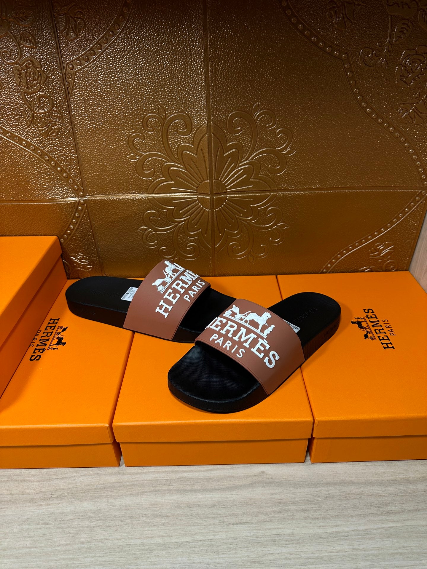 Black slide sandals with tan Hermes Paris logo strap, two sandals side by side