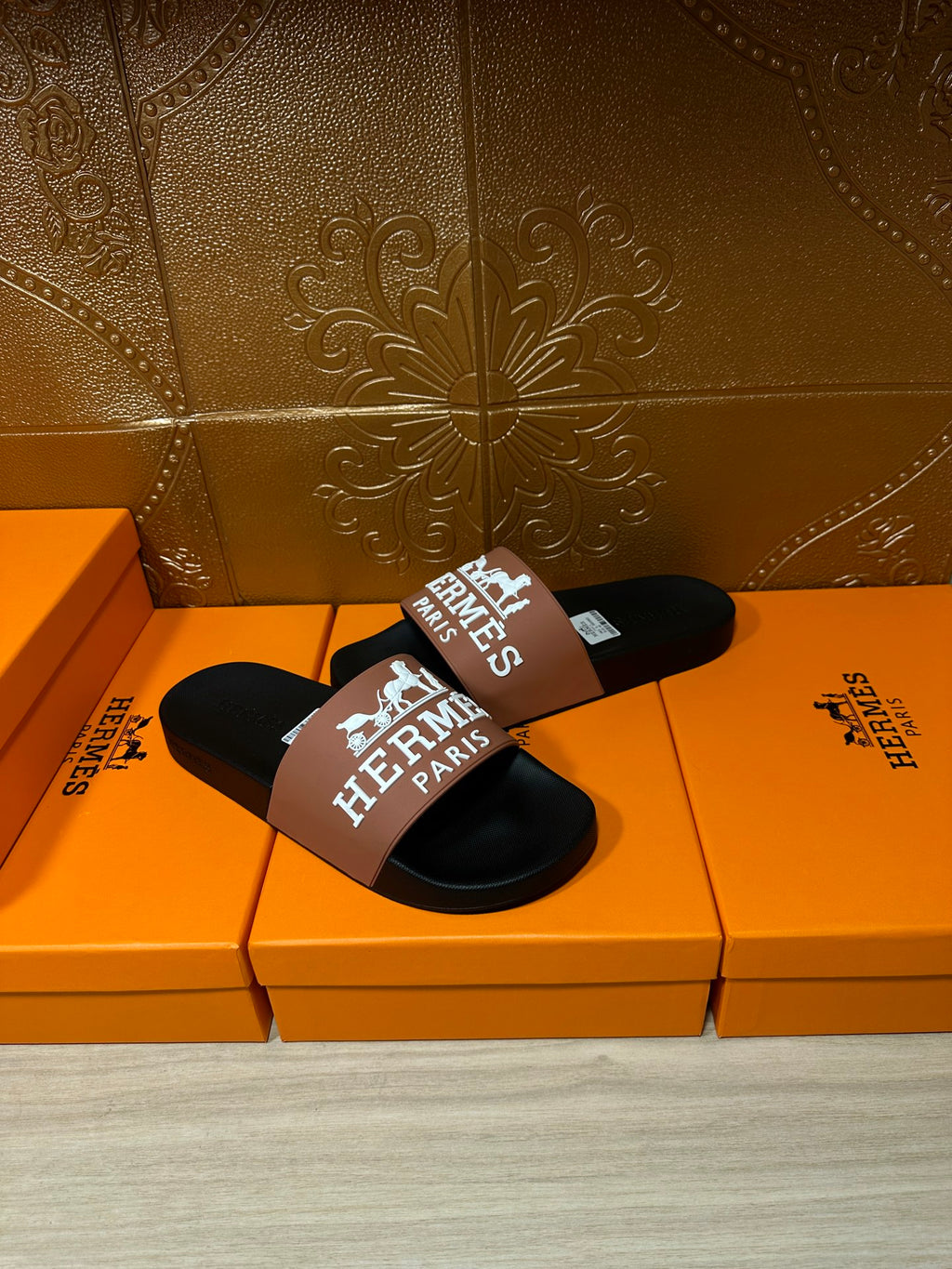 Black Hermes slide sandals with tan logo strap, single sandal on box surface