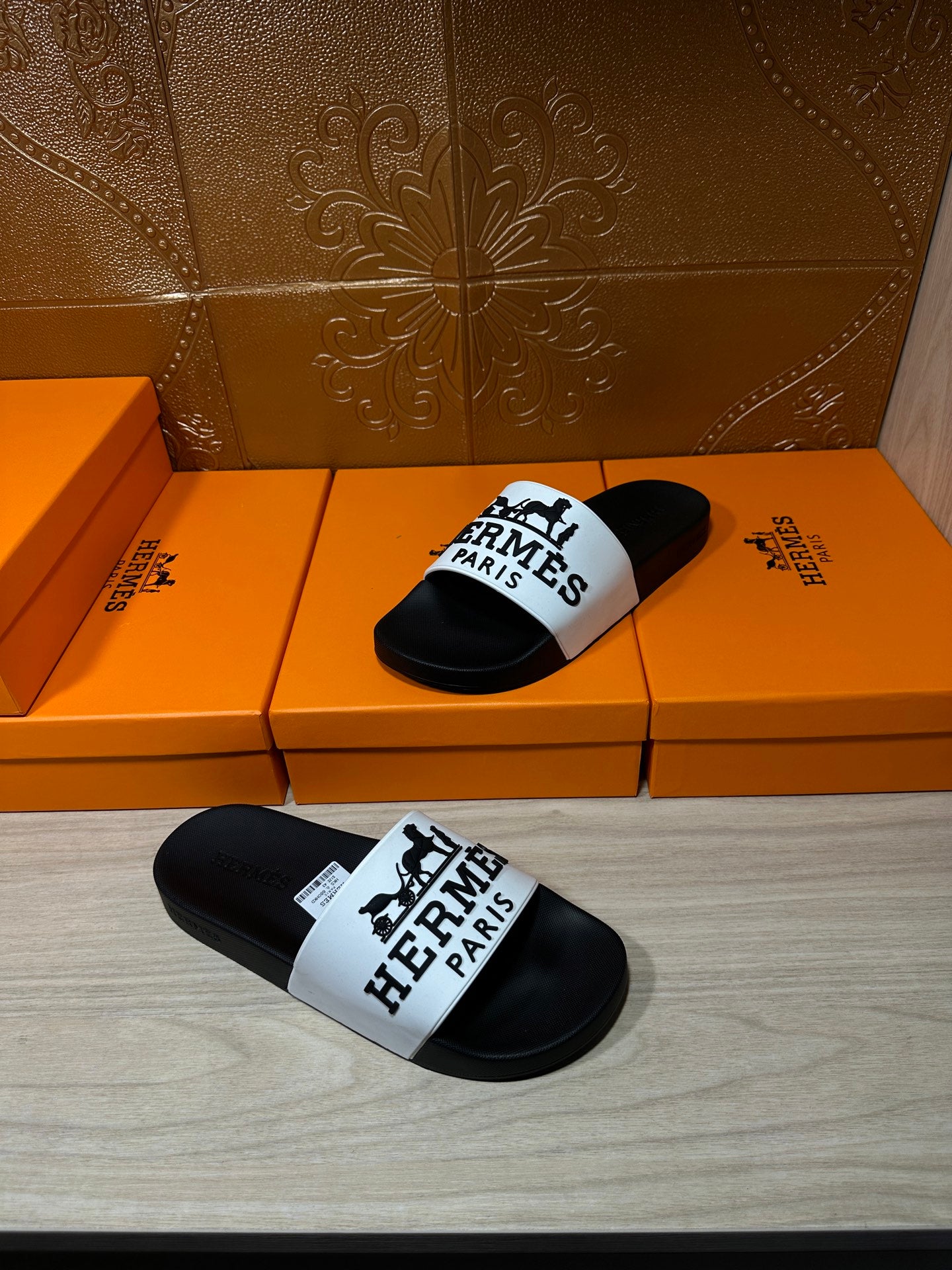 Hermes slide sandals shown at angle: black footbeds with white logo strap