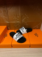 Hermes sandals featuring black slides with a white logo band on the top