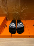 Black slide sandal with blue strap and white "Hermès Paris" lettering