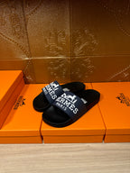 Black slide sandals with blue strap featuring "Hermès Paris" logo and text