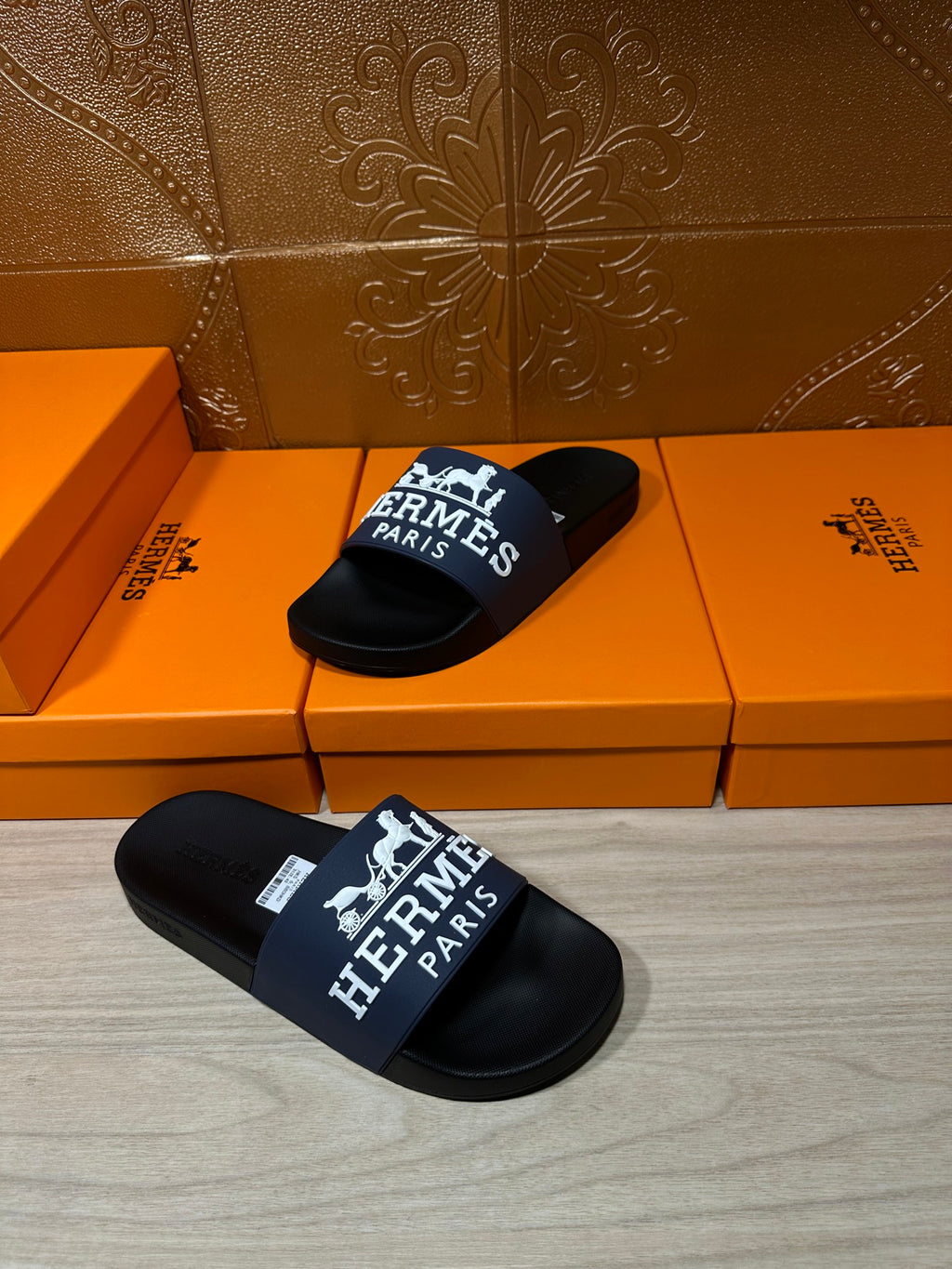Black slide sandal pair with blue strap showing white "Hermès Paris"