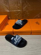 Black slide sandal pair with blue strap showing white "Hermès Paris"