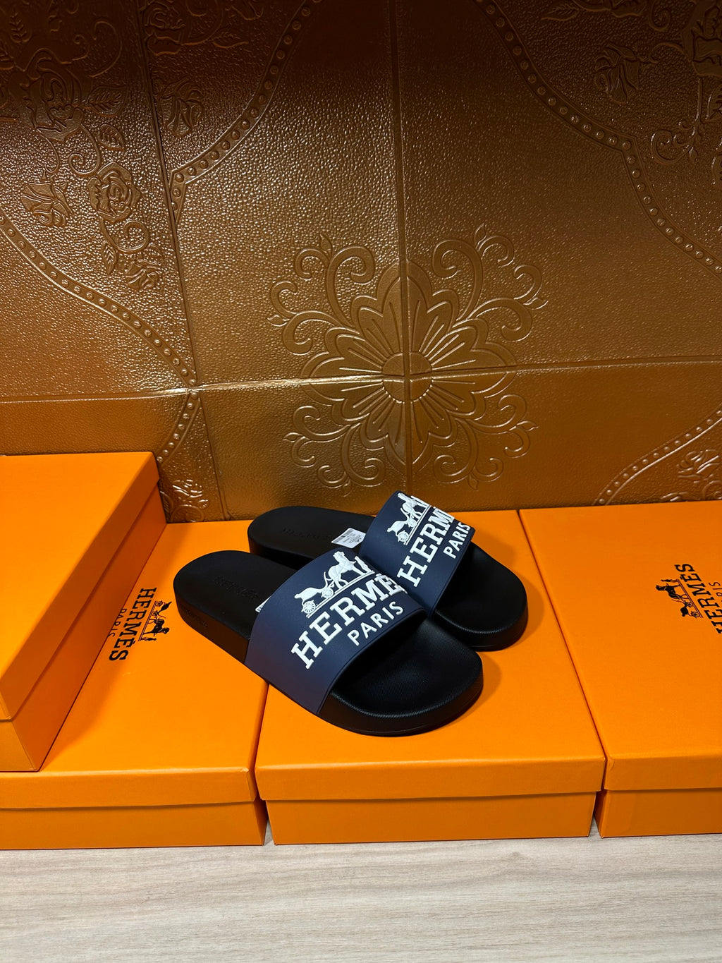 Black slide sandal with blue-and-white strap reading "Hermès Paris"