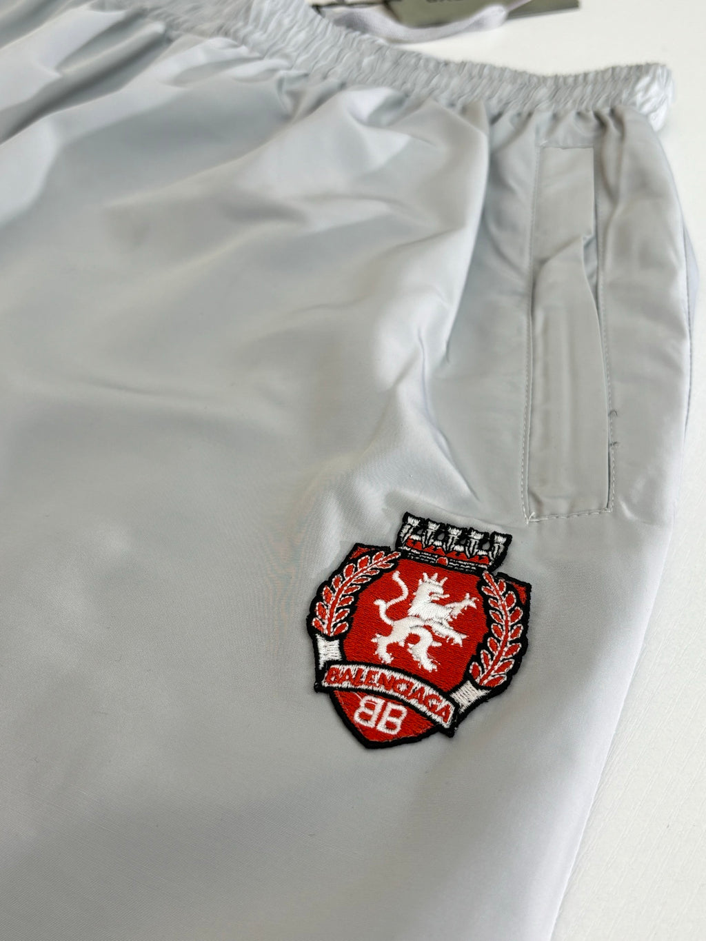 Light blue shorts with red and black Balenciaga crest patch on the front leg
